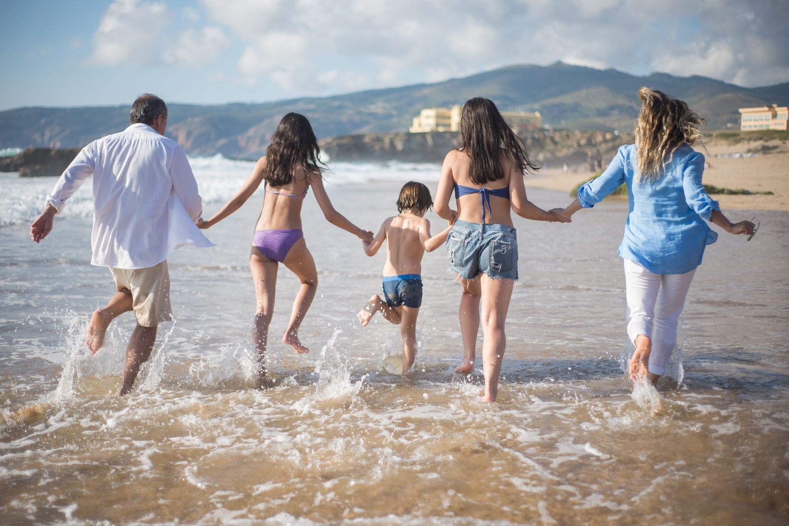 Three generations of cruise travelers running hand in hand into the surf on a beach